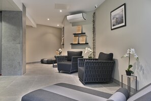 Un espacio de spa con dos sillones negros acolchados, una mesita pequeña y una orquídea en maceta.