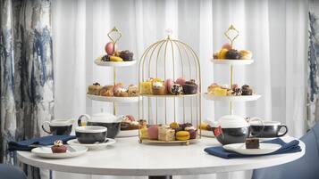 A three-tiered dessert stand with various pastries and macarons, accompanied by teapots and cups on a round table.