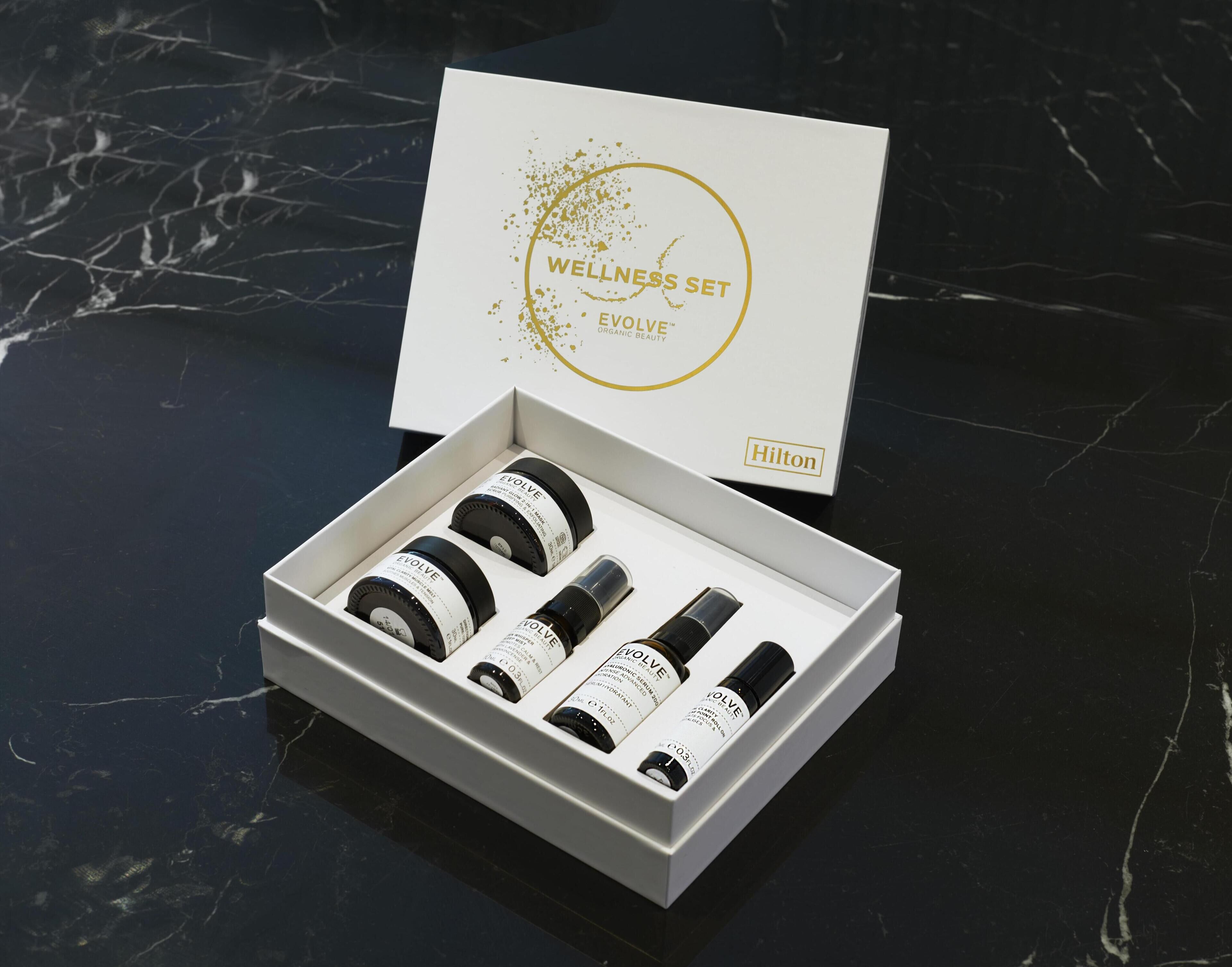 A white box with a gold logo and text, containing four black bottles and a white box with text.