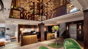 A hotel lobby with a reception desk, green chairs, a staircase, and a decorative ceiling.