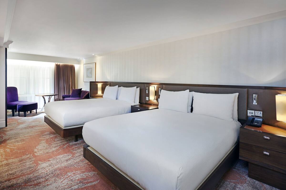 Una camera d'albergo con due letti, una scrivania, una sedia e una finestra con tende.