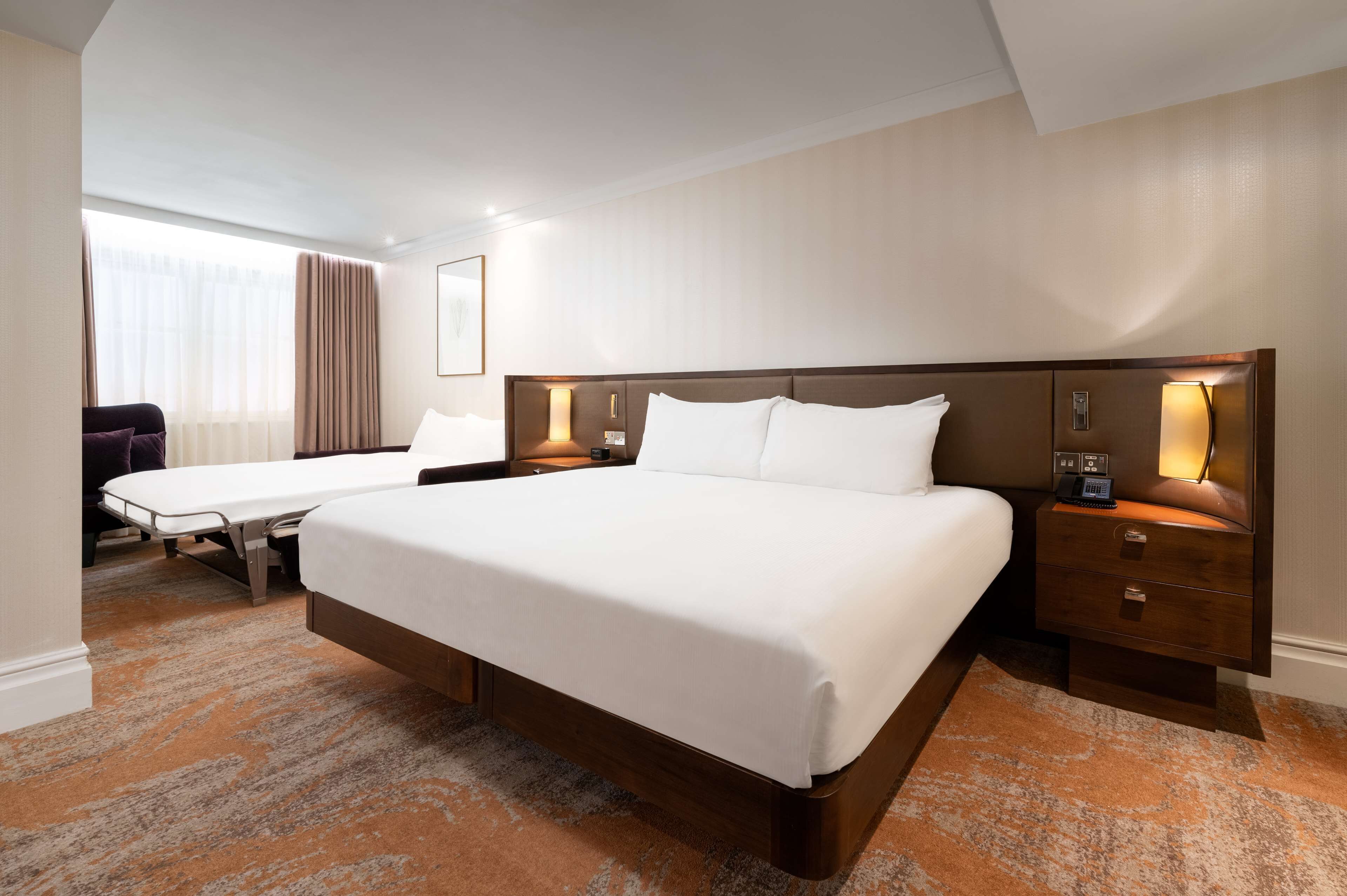 Una camera d'albergo con un letto grande, comodini con lampade, una scrivania e una sedia.