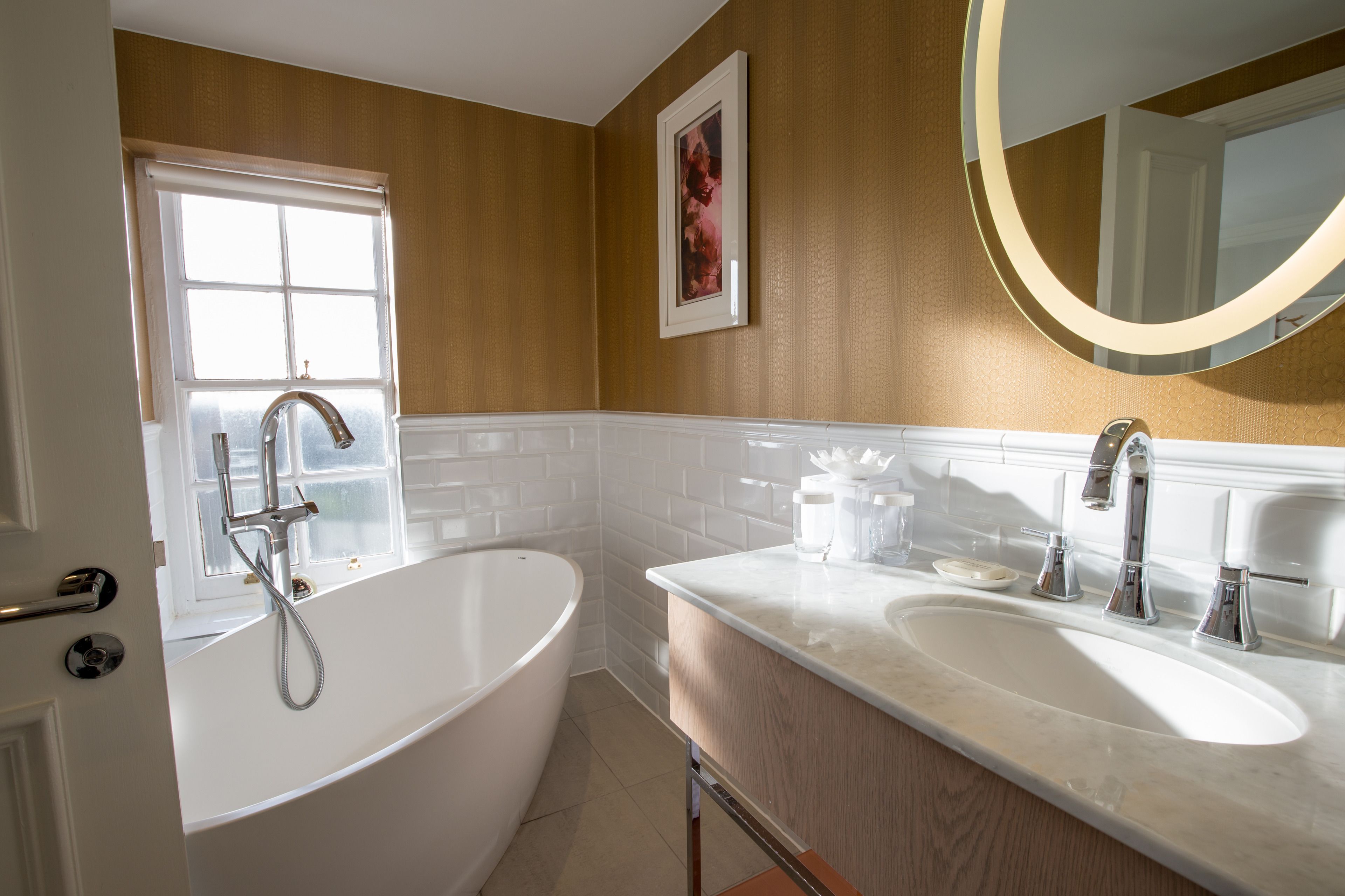 A bathroom with a freestanding bathtub, two sinks, a large mirror, and a window with a view.