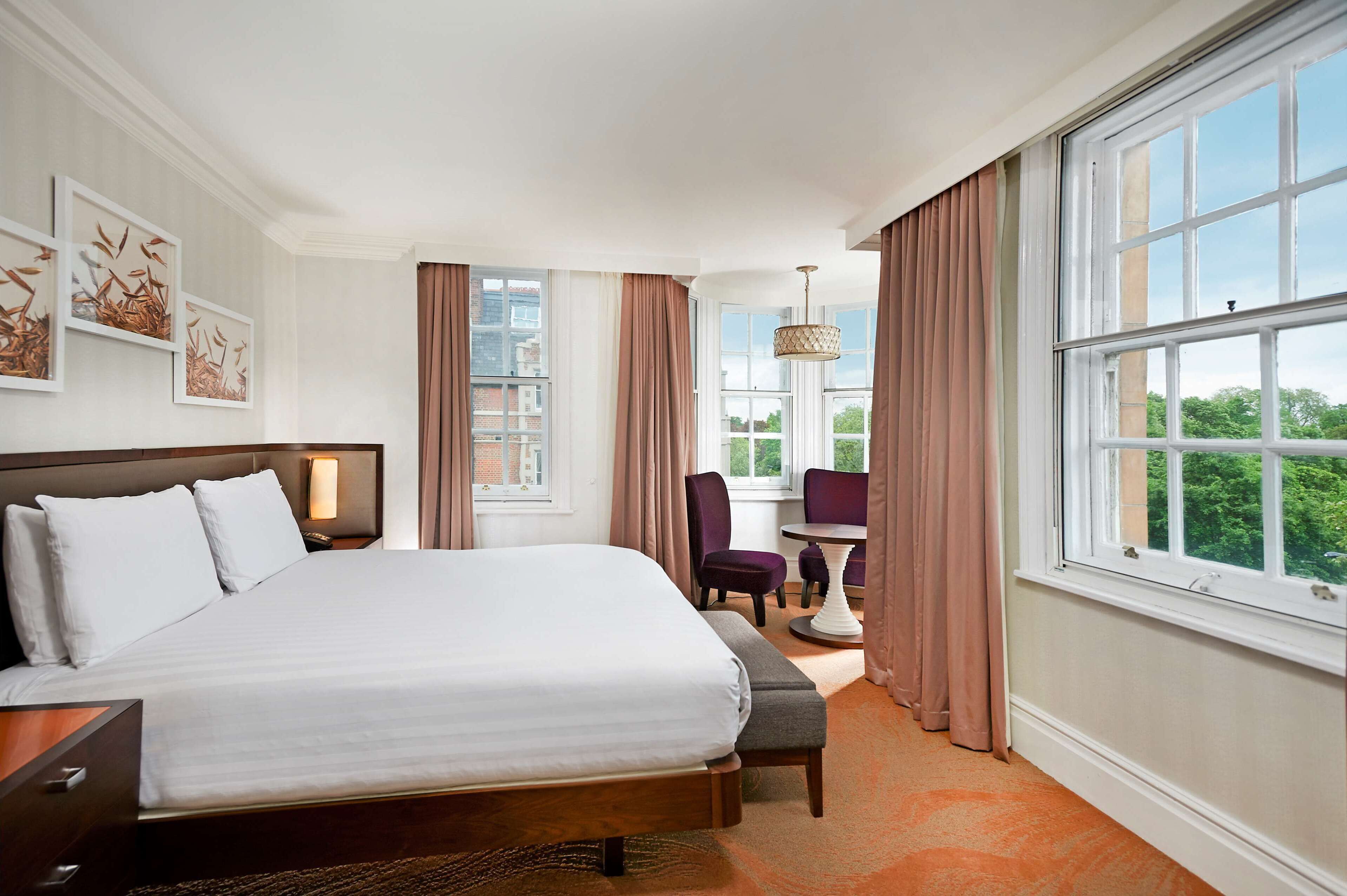 A hotel room with a large bed, a desk, a chair, and a view of the city through the window.