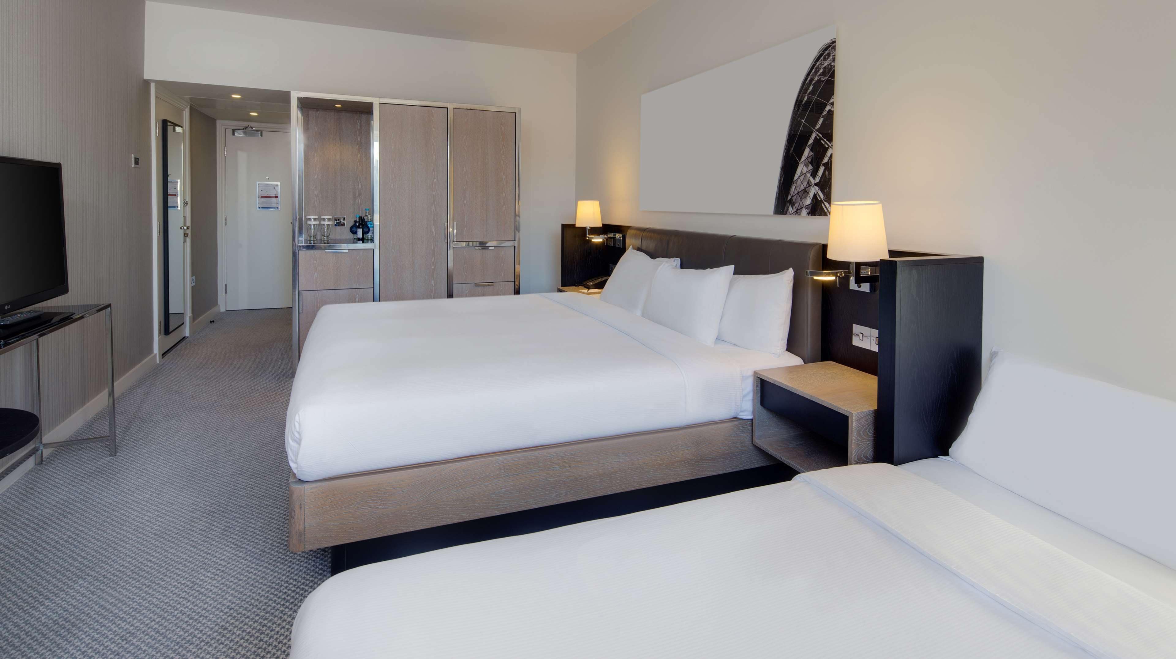 A hotel room with two beds, a TV, a desk with a lamp, and a bathroom visible through an open door.