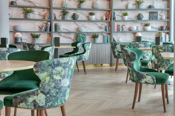 A modern interior with green upholstered chairs, marble shelves with plants and books, and wooden flooring.