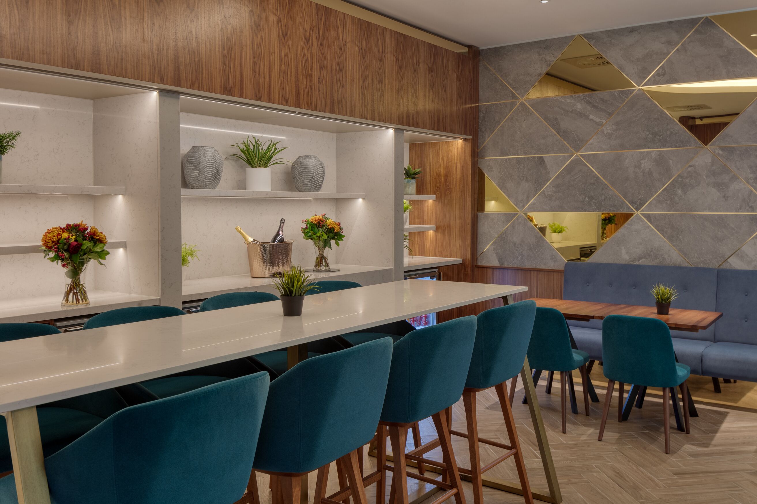 A modern bar area with a long counter, teal chairs, and wooden accents.