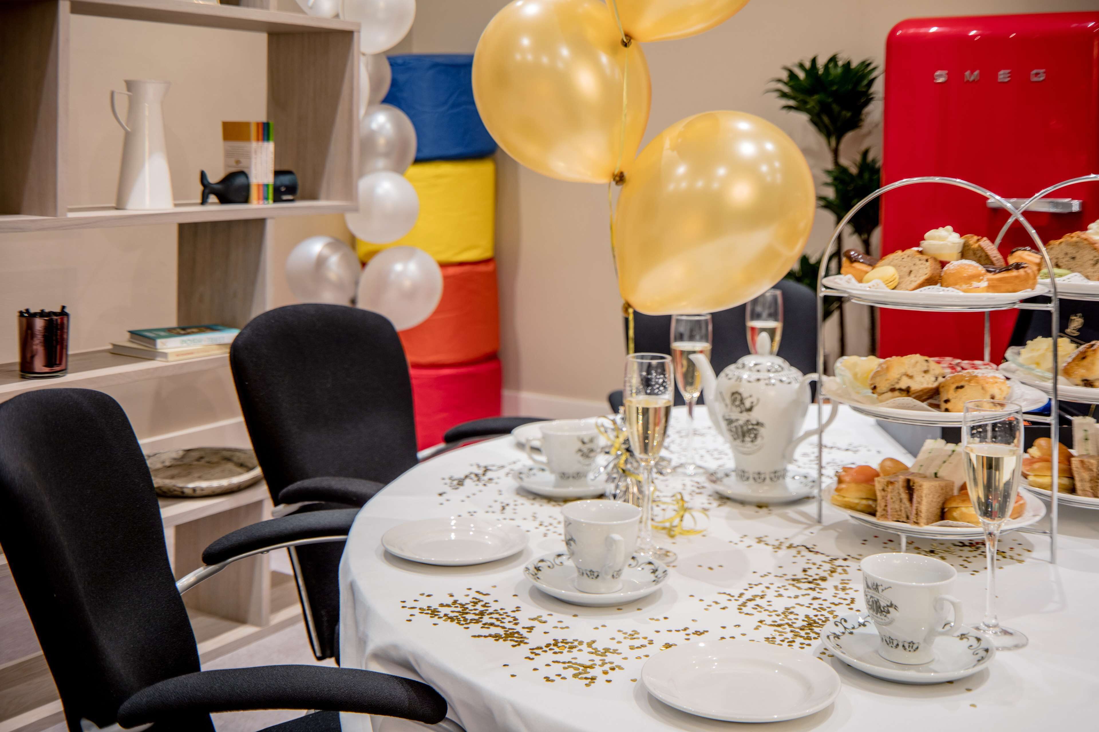 A table set for a tea party with white teacups, saucers, and a tiered tray of pastries.