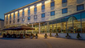 Un hotel con fachada moderna, ventanas amplias y un área de estar al aire libre con sombrillas.