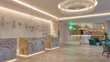 A modern reception area with marble counters, a chandelier, and green chairs.