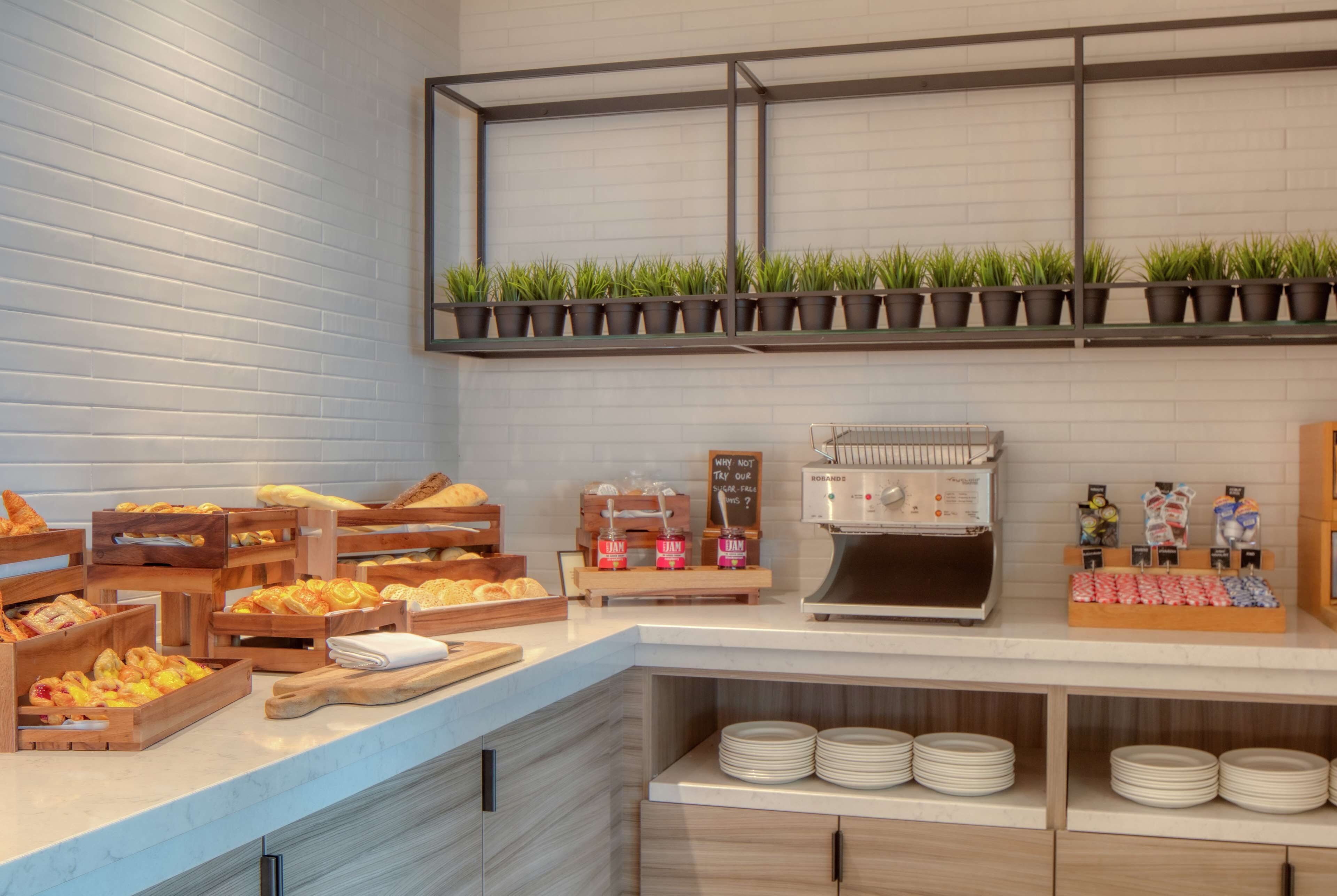 Un bufé de desayuno con diversas opciones de comida, una máquina de café y una estantería con plantas en macetas.