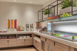 A buffet area with a variety of food items, condiment dispensers, and a glass display case. - Hilton London Angel Islington (London)