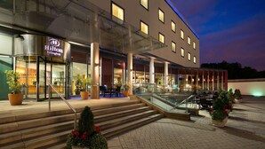 Una entrada de hotel moderna con fachada de vidrio, zona de estar al aire libre y una escalera que lleva a la entrada.