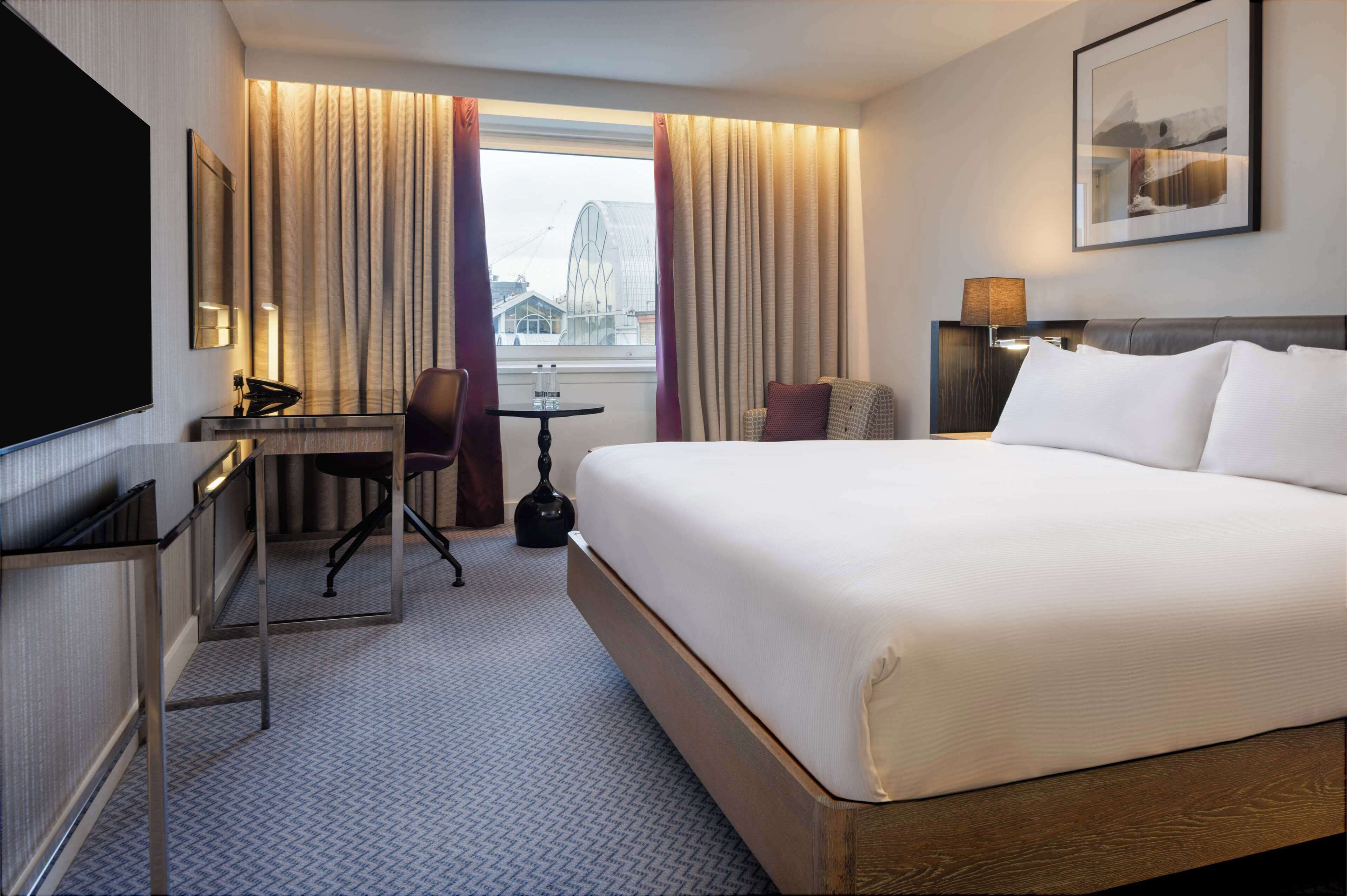 A hotel room with a large bed, a desk with a chair, a TV, and a window with curtains.