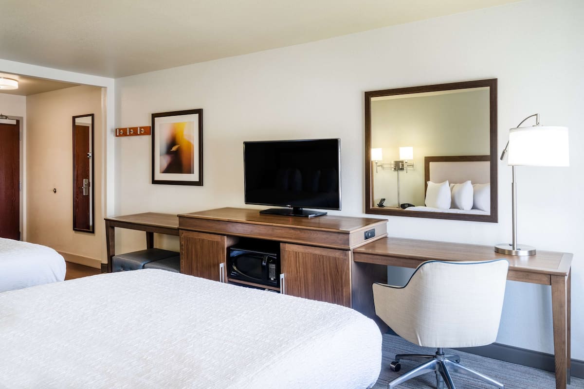 A hotel room with a bed, a desk with a television, a chair, a microwave, and a large mirror.