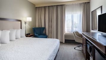 Quarto de hotel com uma cama grande, escrivaninha, cadeira, televisão e janela com cortinas.