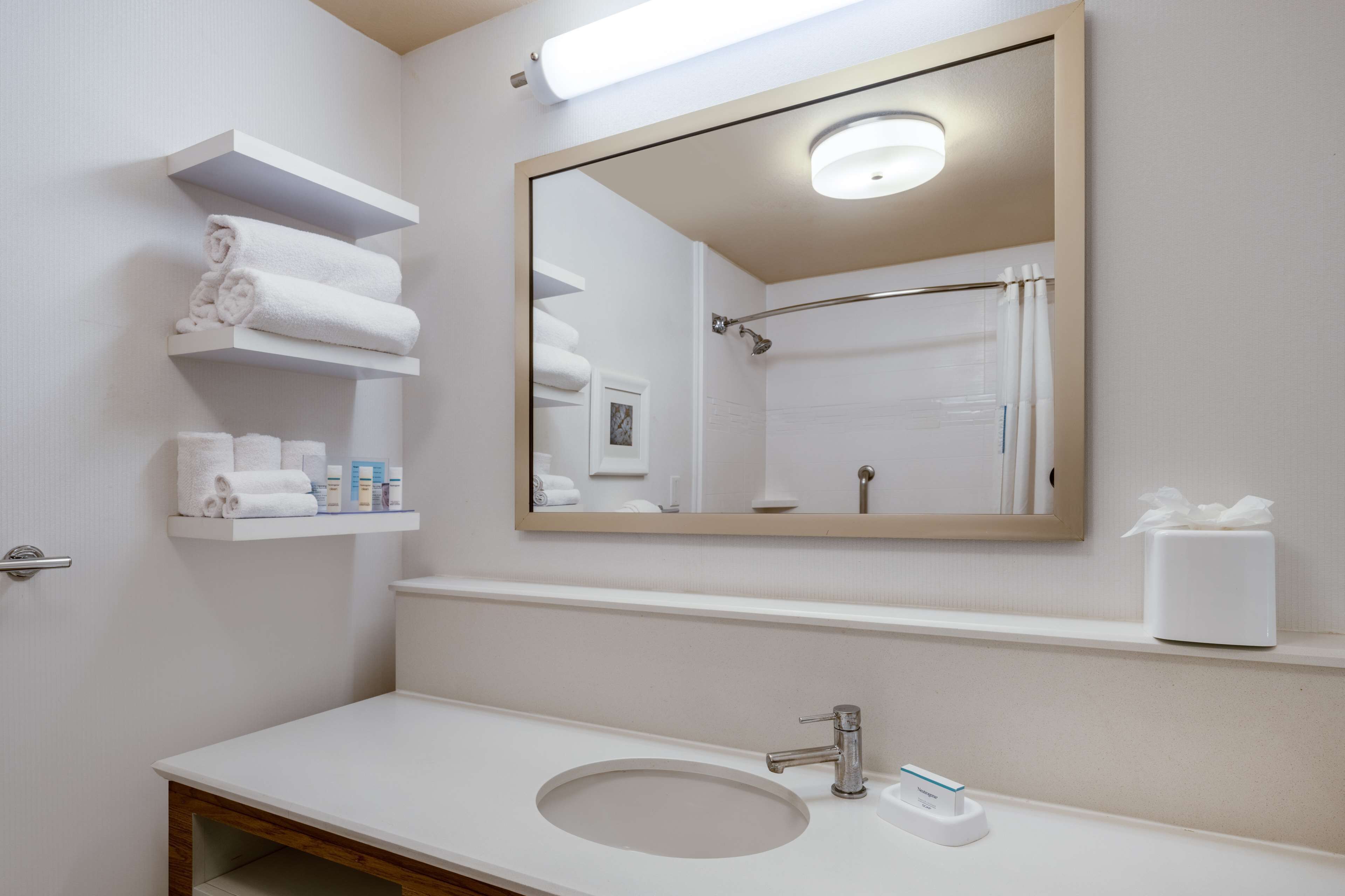 A bathroom with a white sink, a mirror, and shelves with towels and toiletries.