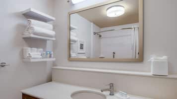 A bathroom with a white sink, a mirror, and shelves with towels and toiletries.