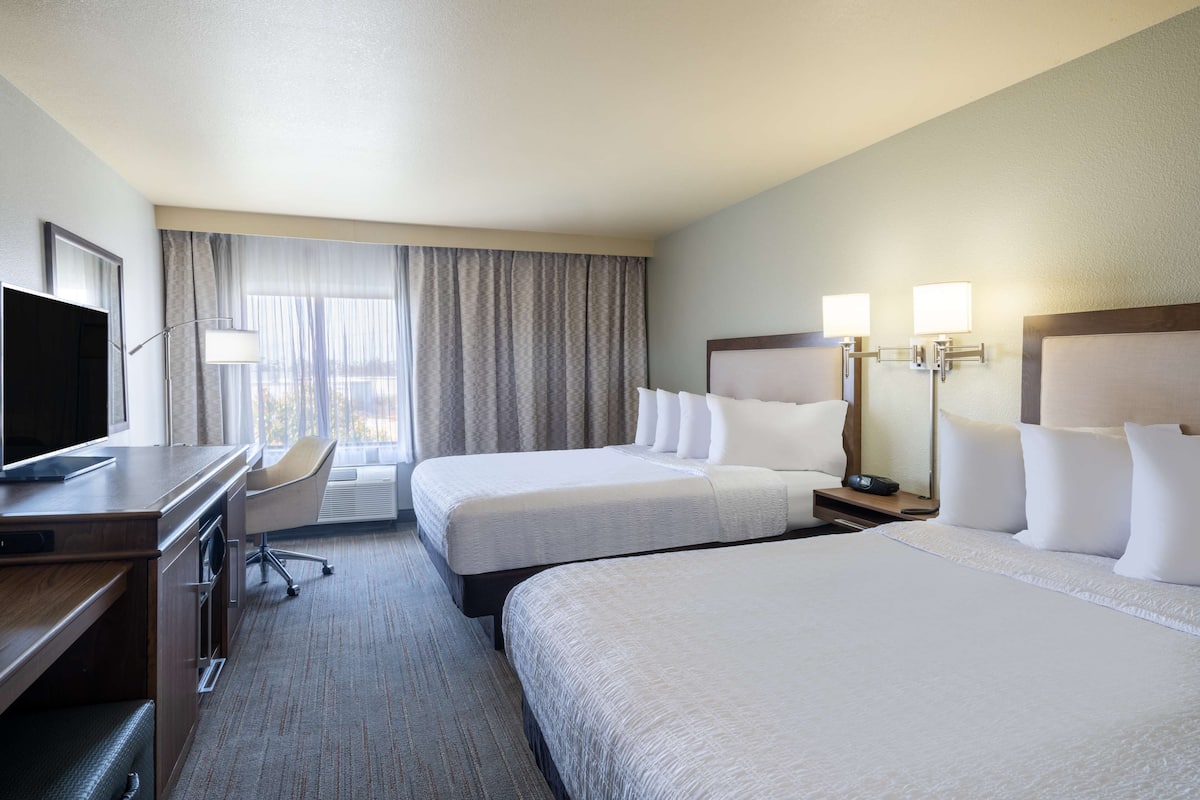 A hotel room with two beds, a desk, a TV, and a window with curtains.