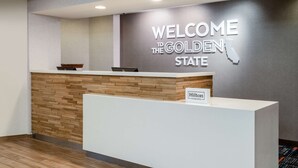 A reception desk with a "Welcome to the Golden State" sign, a "Hilton Honors" sign, and a wooden panel design. - Hampton Inn by Hilton Irvine East - Lake Forest (Foothill Ranch)