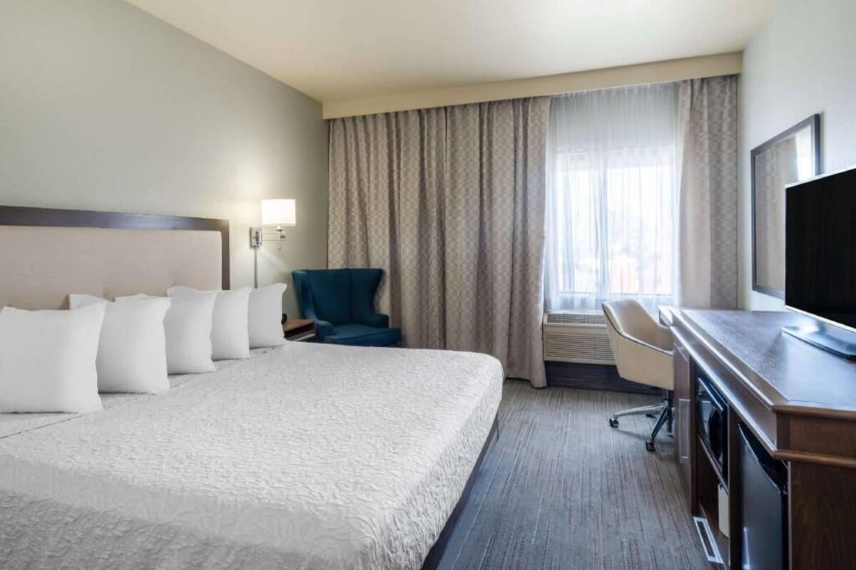 A hotel room with a large bed, a desk, a chair, a television, and a window with curtains.