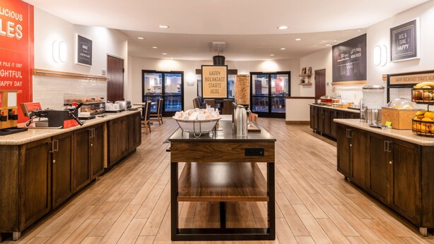 A modern kitchen with wooden cabinets, a central island, and breakfast items on the counter. - Hampton Inn by Hilton Irvine East - Lake Forest (Foothill Ranch)
