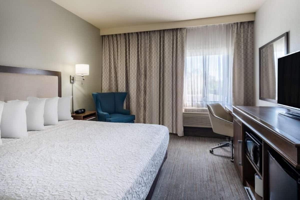 A hotel room with a large bed, a desk, a chair, a television, and a window with curtains.