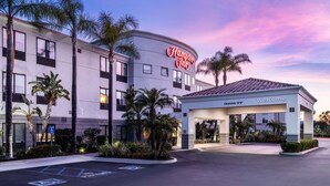 A Hampton Inn hotel with a clear entrance, a parking area, and a sign indicating a 12' clearance. - Hampton Inn by Hilton Irvine East - Lake Forest (Foothill Ranch)