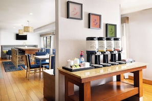 A hotel room with a breakfast bar, coffee makers, and a seating area with chairs and a table.