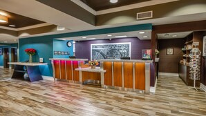 A reception area with a wooden floor, a reception desk, a clock, and a wall with framed pictures and a large bicycle poster. - Hampton Inn San Francisco Airport (South San Francisco)