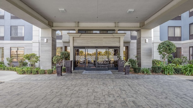 A modern building entrance with a covered walkway, large glass doors, and potted plants. - Hampton Inn San Francisco Airport (South San Francisco)