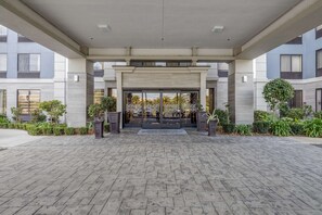 A modern building entrance with a covered walkway, large glass doors, and potted plants. - Hampton Inn San Francisco Airport (South San Francisco)