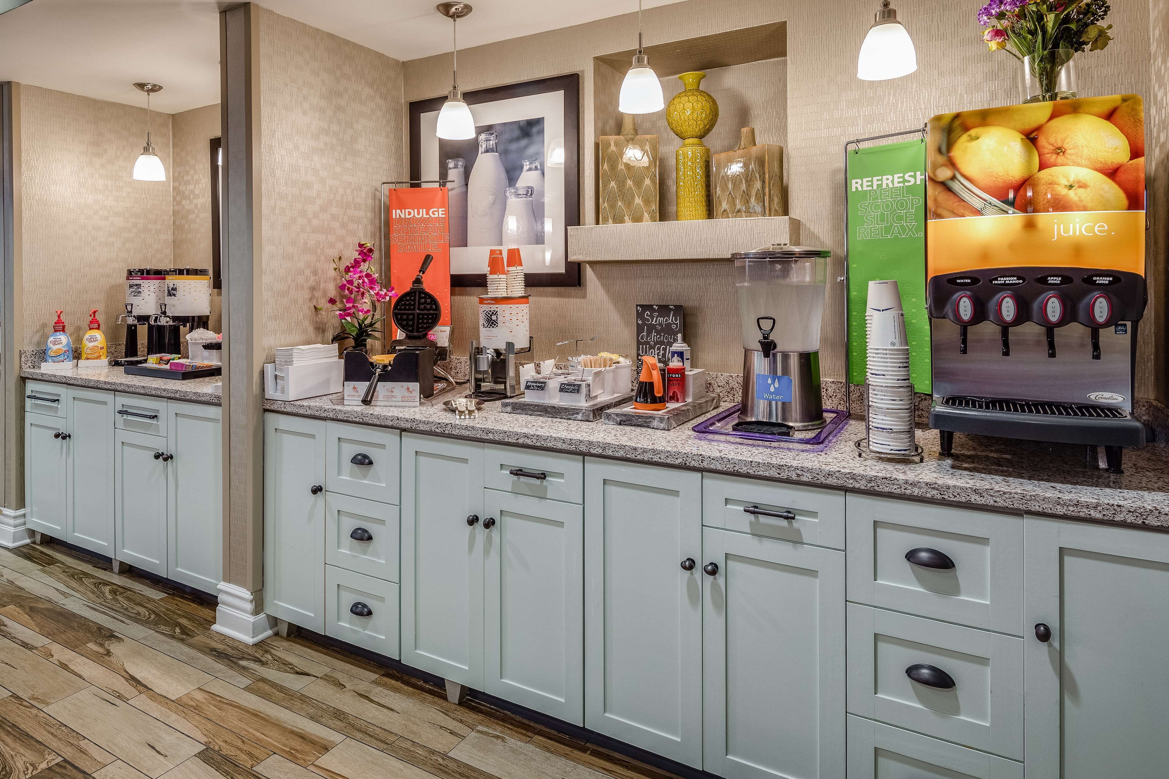 A hotel reception area with a coffee machine, juice dispenser, and various amenities like condiments and napkins.