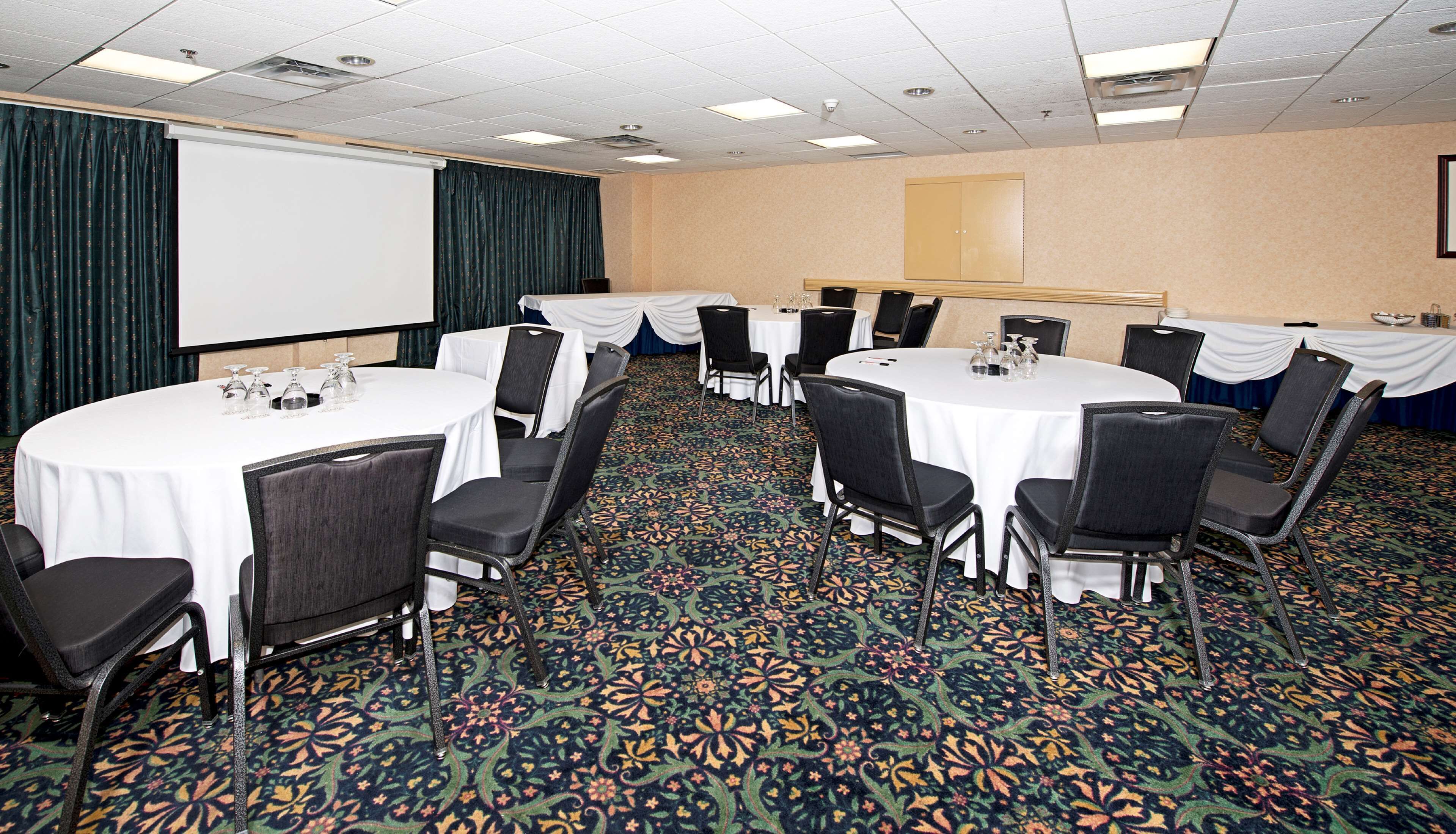 Un salón de conferencias con varias mesas redondas, sillas negras y una pantalla de proyector.