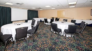 Un salón de conferencias con varias mesas redondas, sillas negras y una pantalla de proyector.