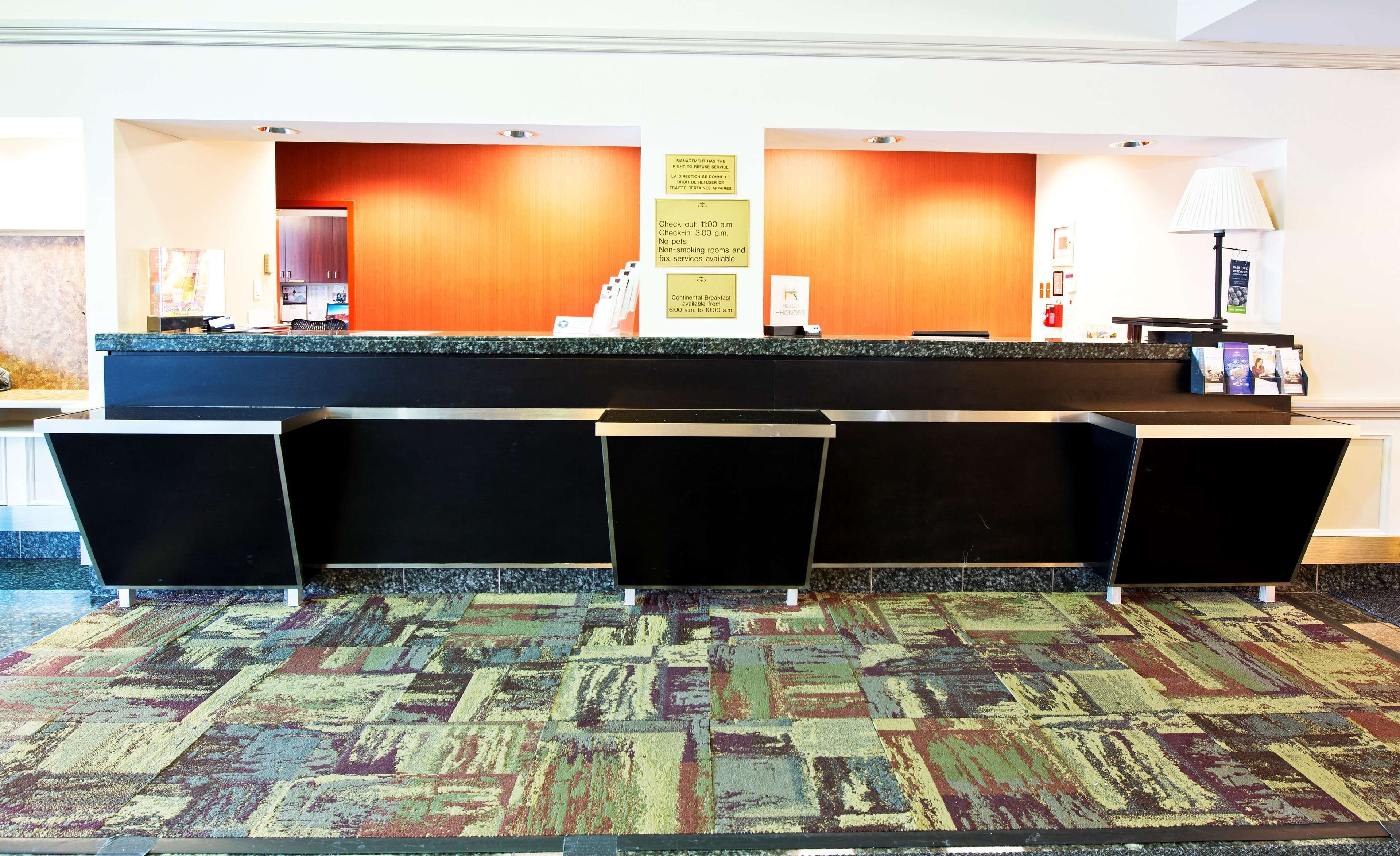 A hotel reception area with a check-in counter, a continental breakfast sign, and a no-pets policy notice.