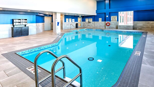 Une piscine intérieure avec un sol carrelé, une échelle en métal et des panneaux de signalisation de sécurité.
