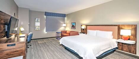 A hotel room with a large bed, a desk with a computer, a chair, a TV, and artwork on the walls.