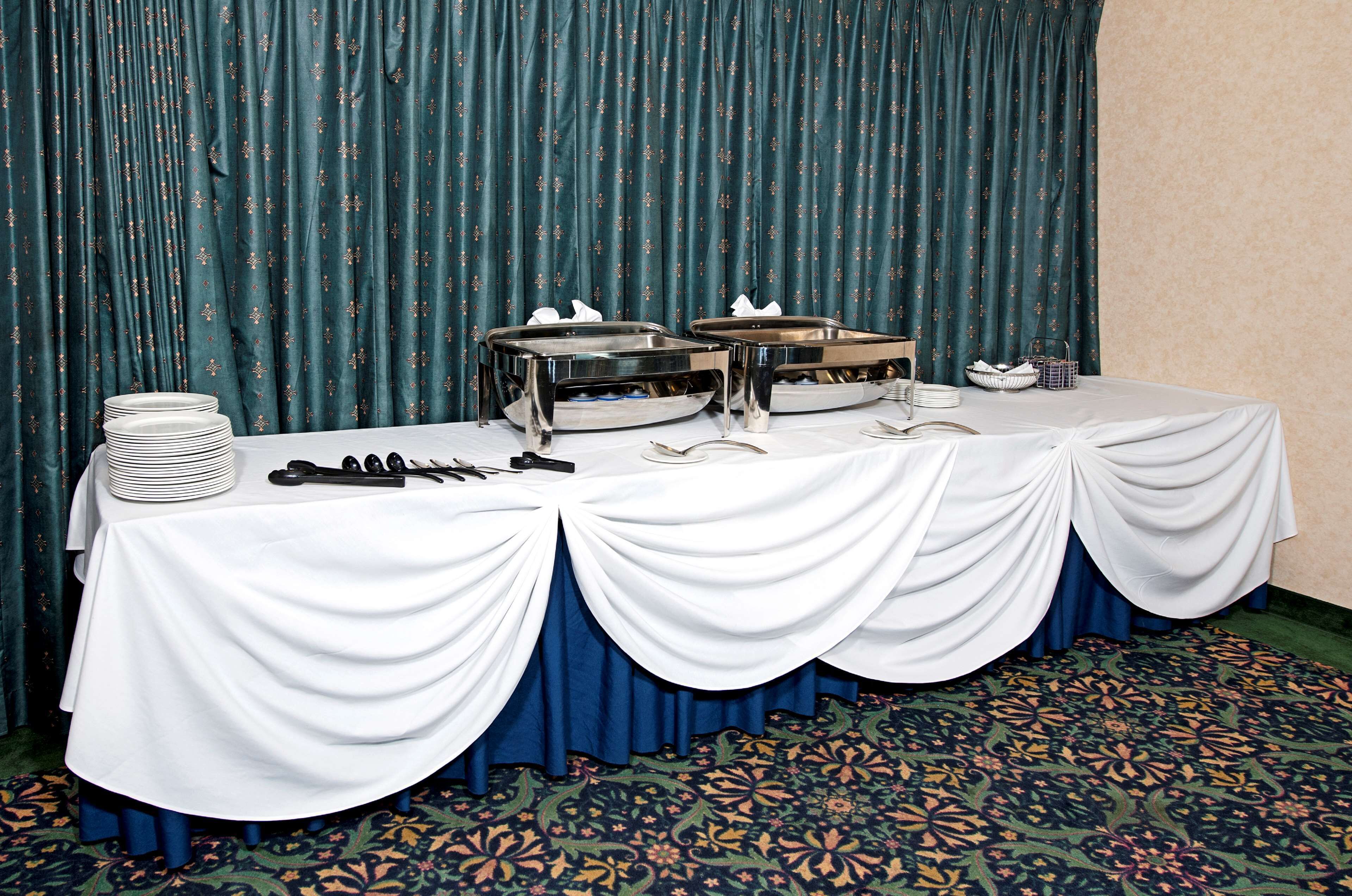 A buffet table with white tablecloths, silver serving trays, and stacked plates.