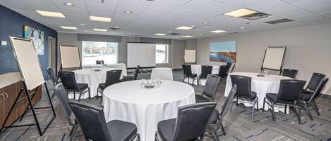 A conference room with multiple round tables, black chairs, white tablecloths, and presentation screens.