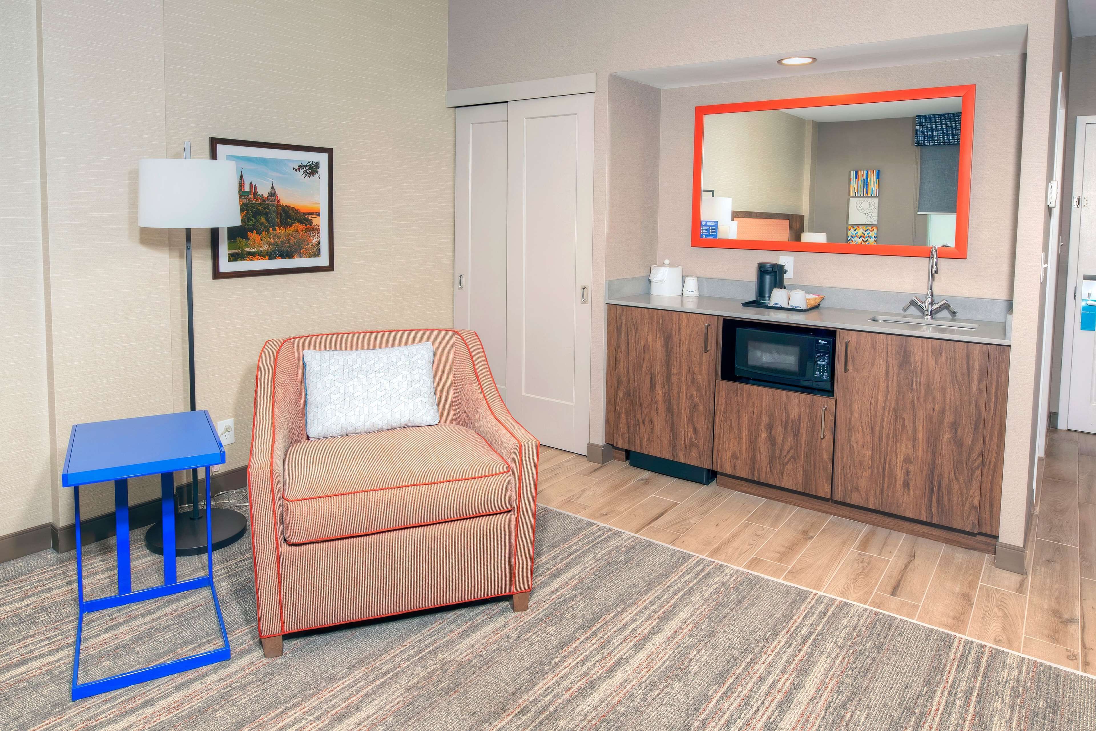 Habitación de hotel con sofá, una mesita, un mueble con lavabo y un espejo con marco rojo.