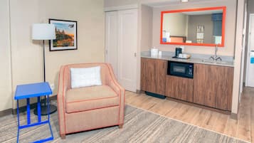 Une chambre d’hôtel avec un canapé, une petite table, un meuble avec un lavabo et un miroir doté d’un cadre rouge.