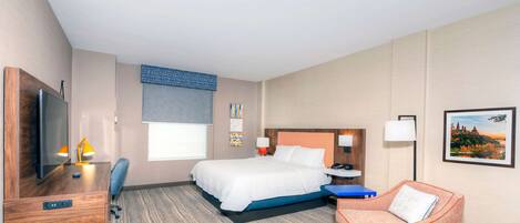 A hotel room with a bed, a desk with a TV, a chair, a sofa, a lamp, and a picture on the wall.