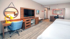 Une chambre d’hôtel comprenant un lit, un bureau avec une chaise, une télévision, un miroir et une petite kitchenette.