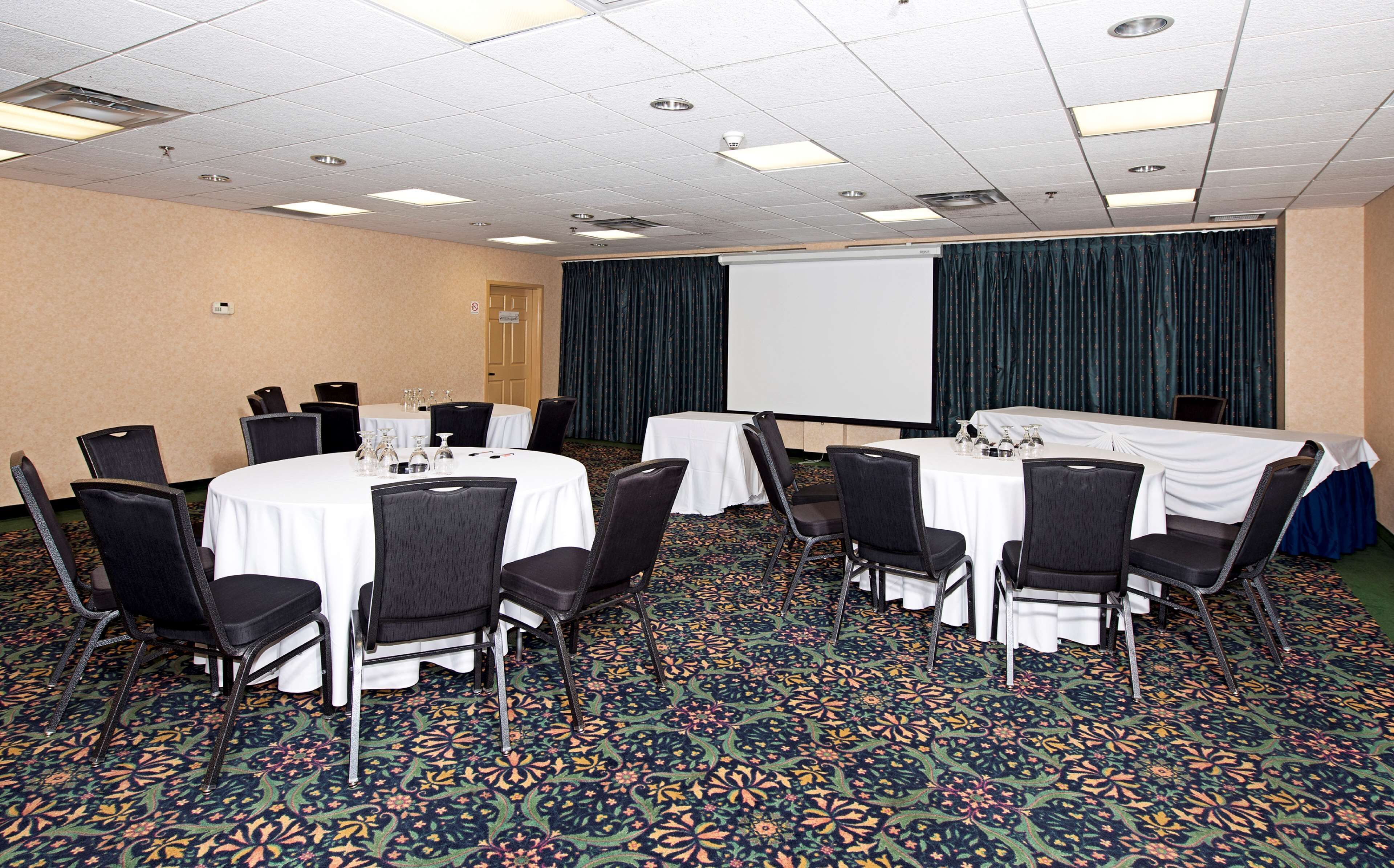 A conference room with round tables, black chairs, and a projector screen.