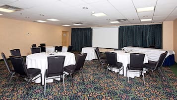 A conference room with round tables, black chairs, and a projector screen.