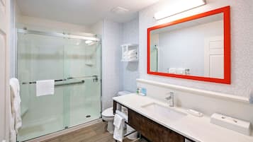 Un baño moderno con ducha de vidrio, un lavamanos blanco con tocador de madera y un espejo grande con marco rojo.
