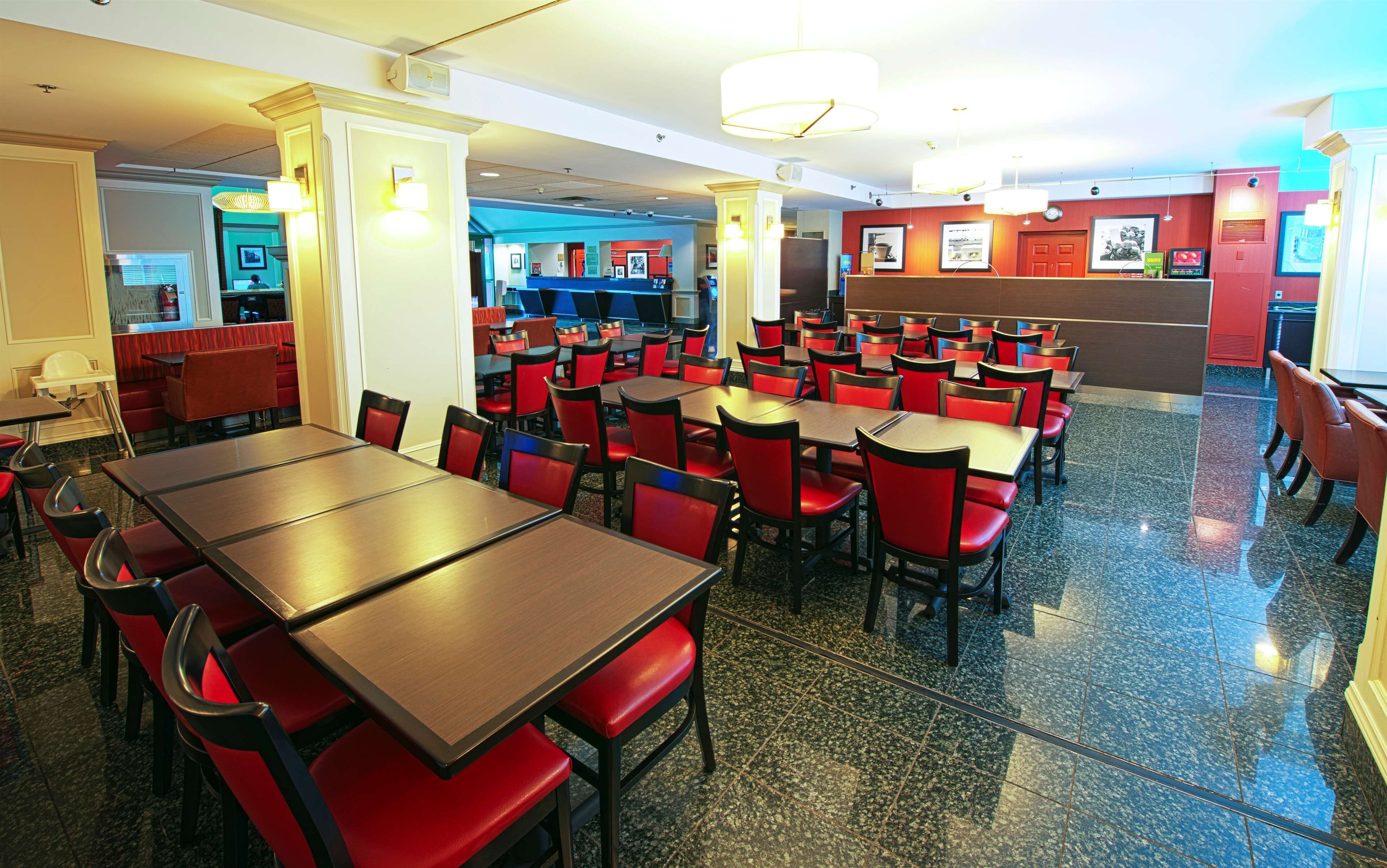 A spacious restaurant with multiple tables and red chairs, a counter area, and a view into another section of the building.