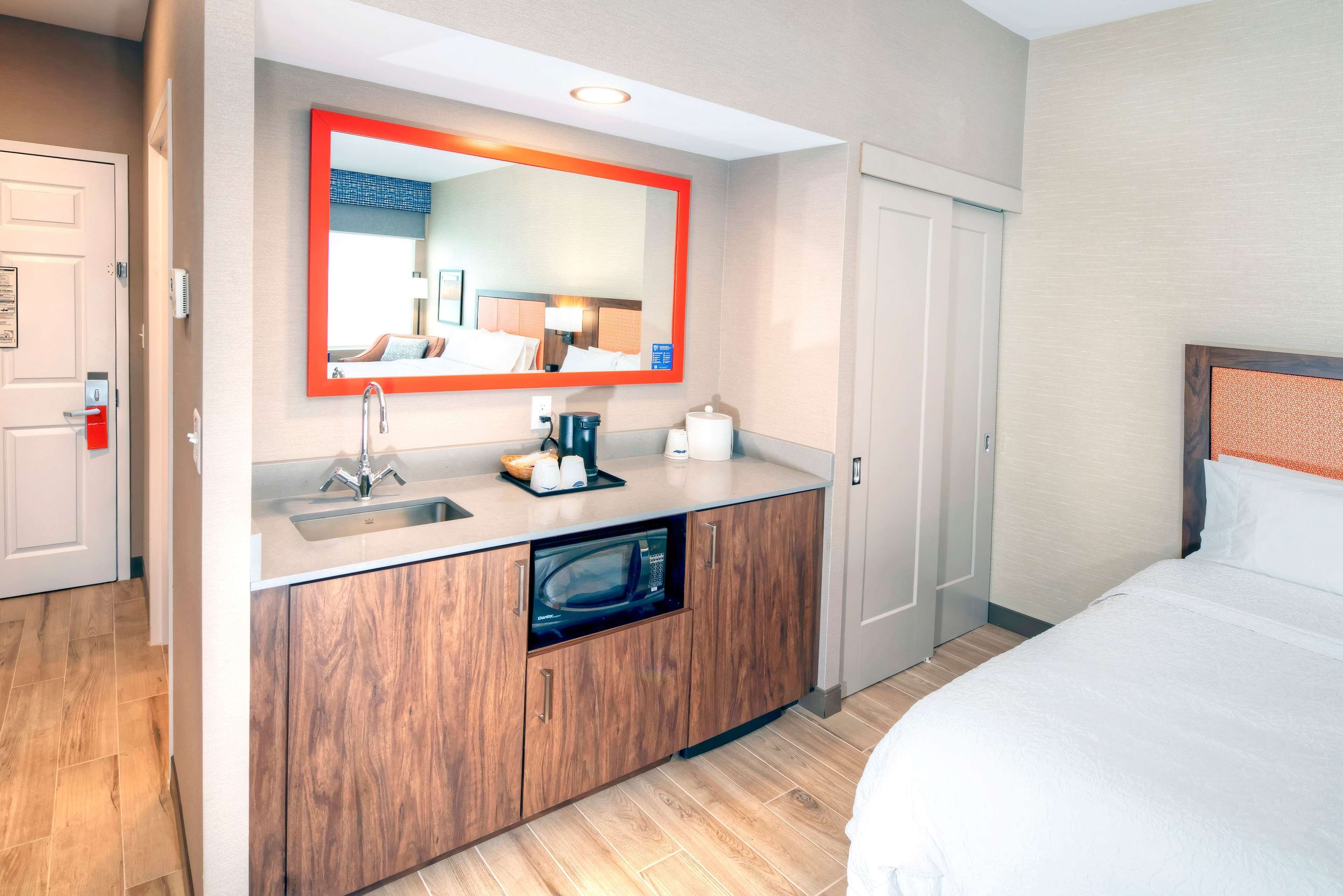 A hotel room with a wooden cabinet, a built-in microwave, a sink, and a bed.
