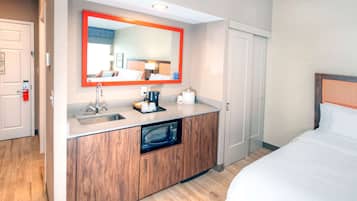 A hotel room with a wooden cabinet, a built-in microwave, a sink, and a bed.